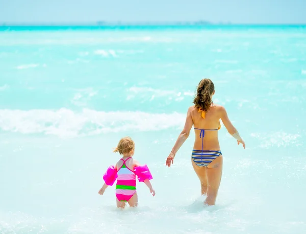 Madre e hija entrando en el mar. visión trasera —  Fotos de Stock