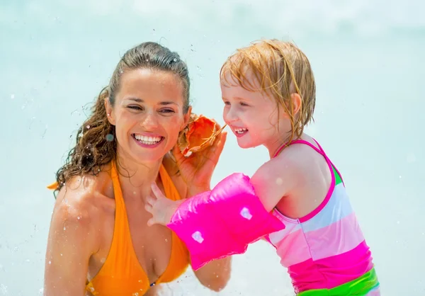 Portrait of mother and baby girl listening sound of sea in shell — Stock Photo, Image