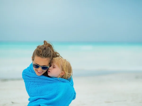 Mamma och baby flicka insvept i handduk sitter på stranden — Stockfoto
