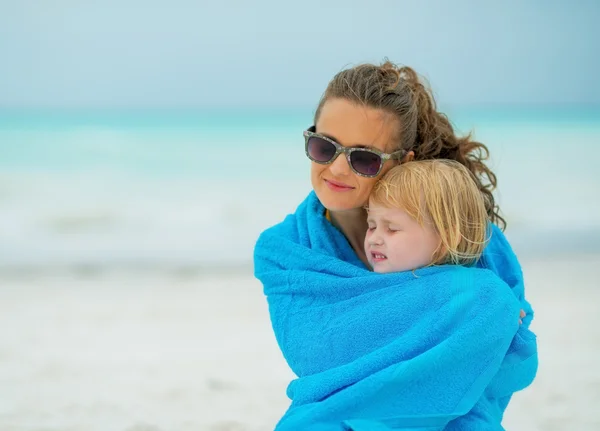 Matka a dítě dívka zabalená v ručníku, sedí na pláži — Stock fotografie