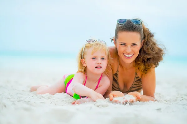 Retrato de madre sonriente y niña acostada en la playa — Foto de Stock