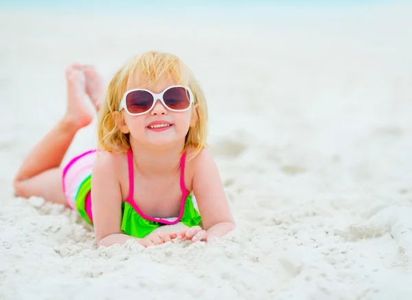 Portrait of baby girl in sunglasses laying on beach — Stock Photo, Image