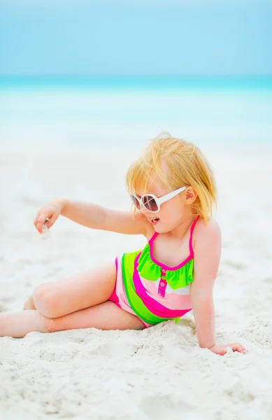 Meisje van de baby in zonnebril spelen met zand op het strand — Stockfoto