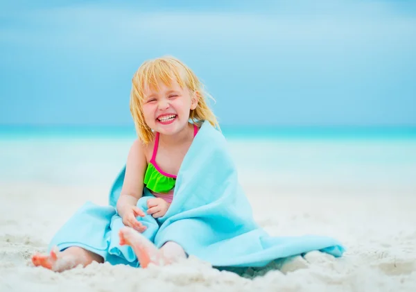 Portrait of smiling baby girl in towel sitting on beach — Stock Photo, Image