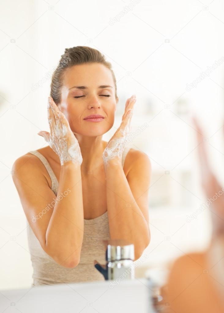 Young woman washing face in bathroom