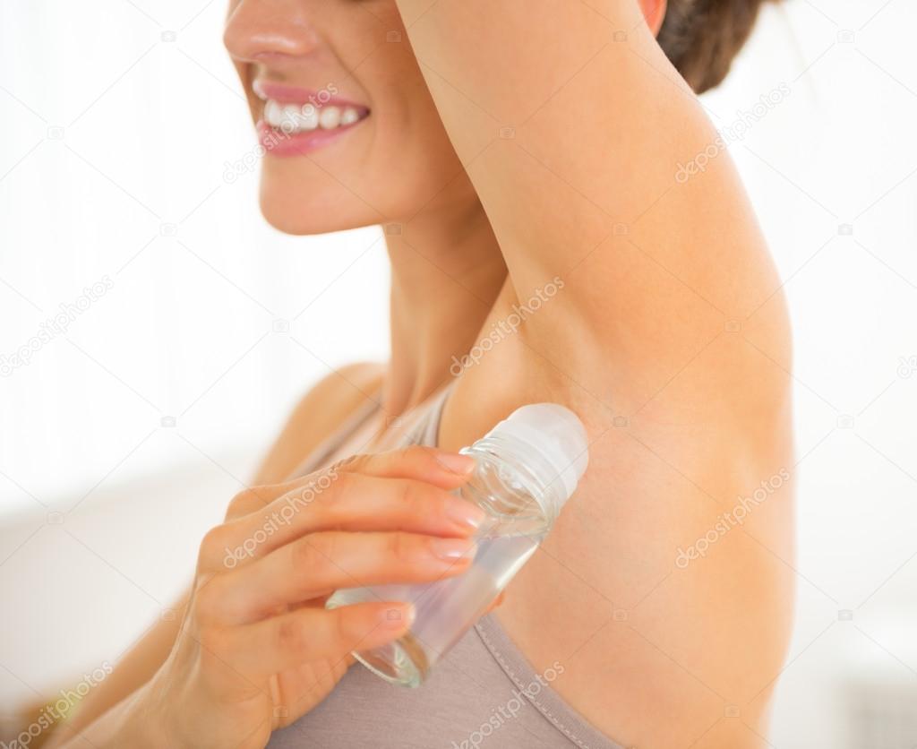 Closeup on happy young woman applying deodorant on underarm