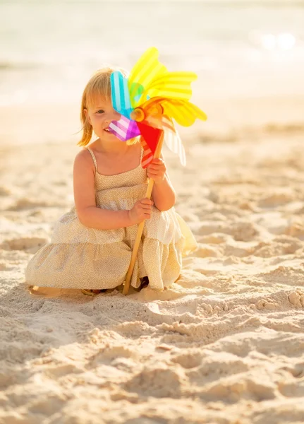 Portrait of happy baby girl with toy windmill on the beach in th — Stock Photo, Image