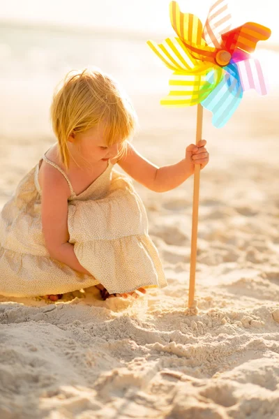 Niña jugando con el juguete colorido molino de viento en la playa en el — Foto de Stock