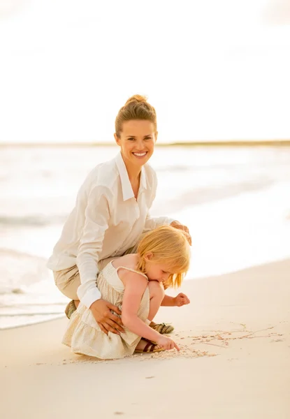 Glückliche Mutter und kleines Mädchen spielen am Abend am Strand — Stockfoto