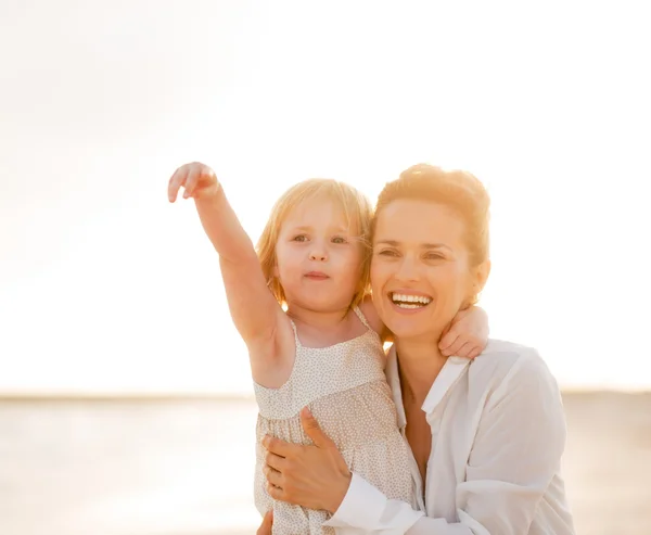 Happy mother and baby girl pointing on copy space on the beach i — Stock Photo, Image