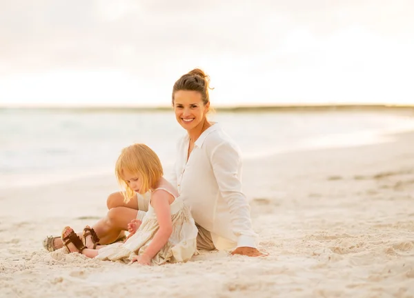 Lykkelig mor og baby pige sidder på stranden om aftenen - Stock-foto