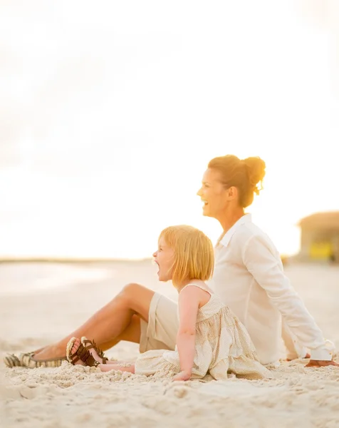 Feliz niña y madre sentadas en la playa por la noche a — Foto de Stock