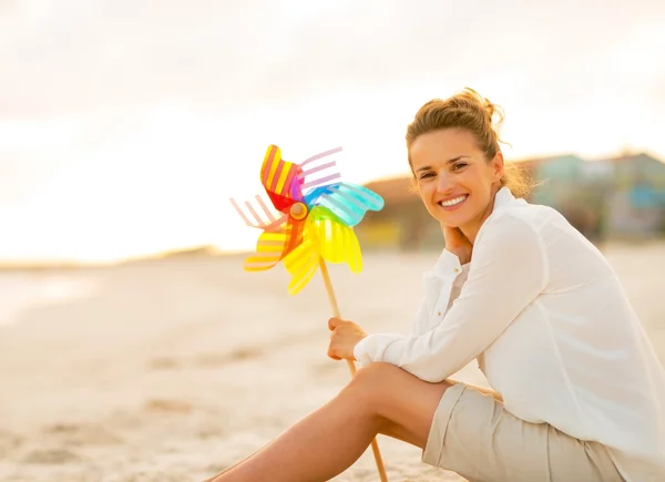 Ung kvinna med färgglada väderkvarnen leksak sitter på stranden i t — Stockfoto