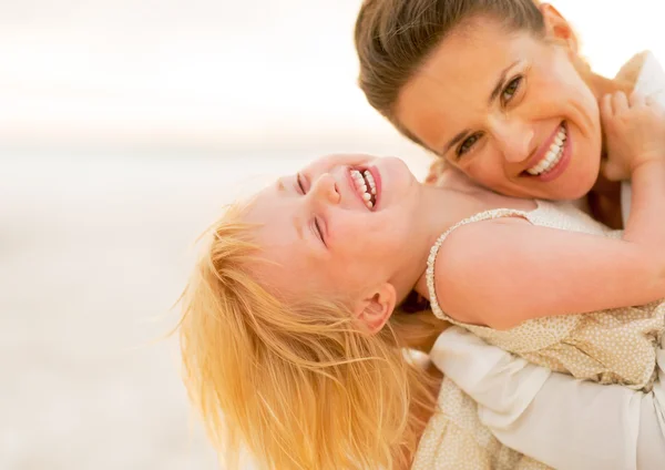 Sorridente madre e bambina si divertono sulla spiaggia in — Foto Stock