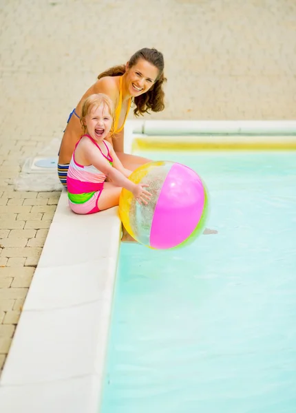 Mãe feliz e bebê menina com bola sentada perto da piscina — Fotografia de Stock