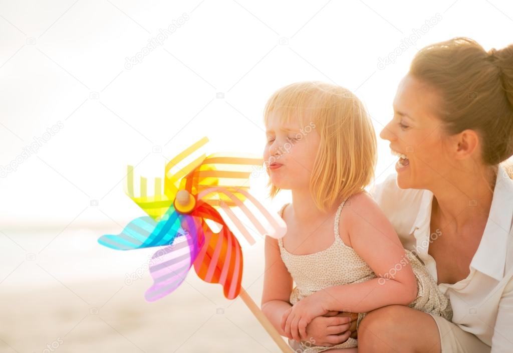 Mother and baby girl playing with colorful windmill toy on the b