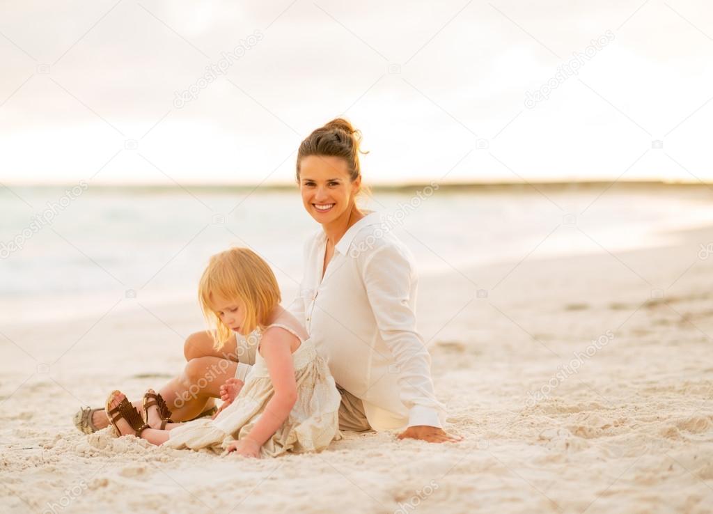 Happy mother and baby girl sitting on the beach in the evening