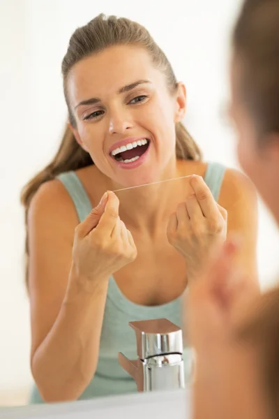 Portret van een jonge vrouw met behulp van tandzijde in badkamer — Stockfoto