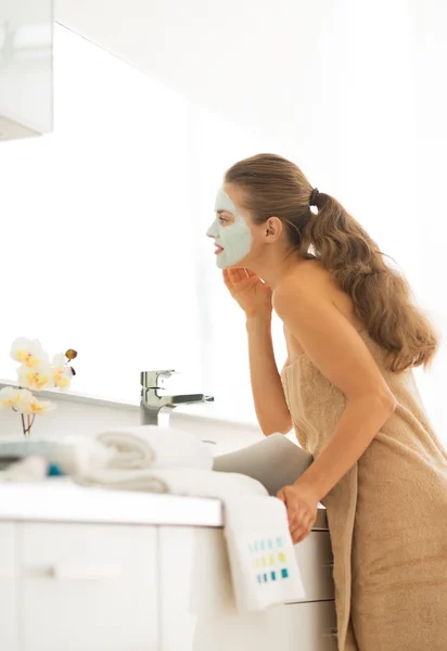 Young woman wearing facial cosmetic mask in bathroom looking in — Stock Photo, Image