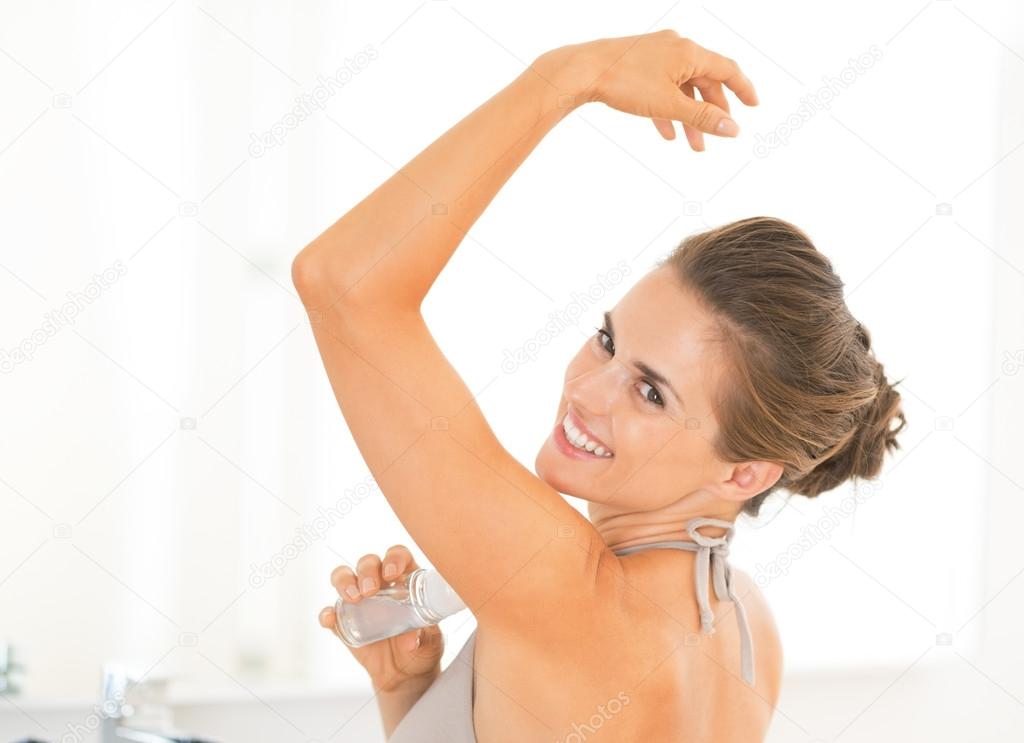 Portrait of happy young woman applying deodorant on underarm