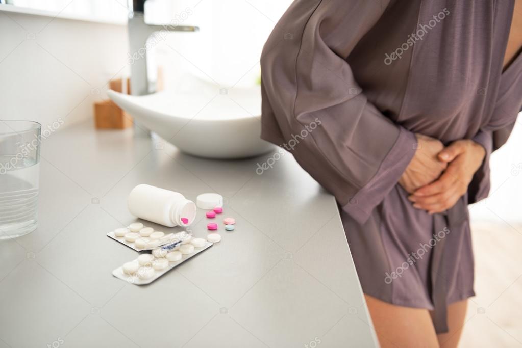 Closeup on pills on table and young woman with stomach pain in b