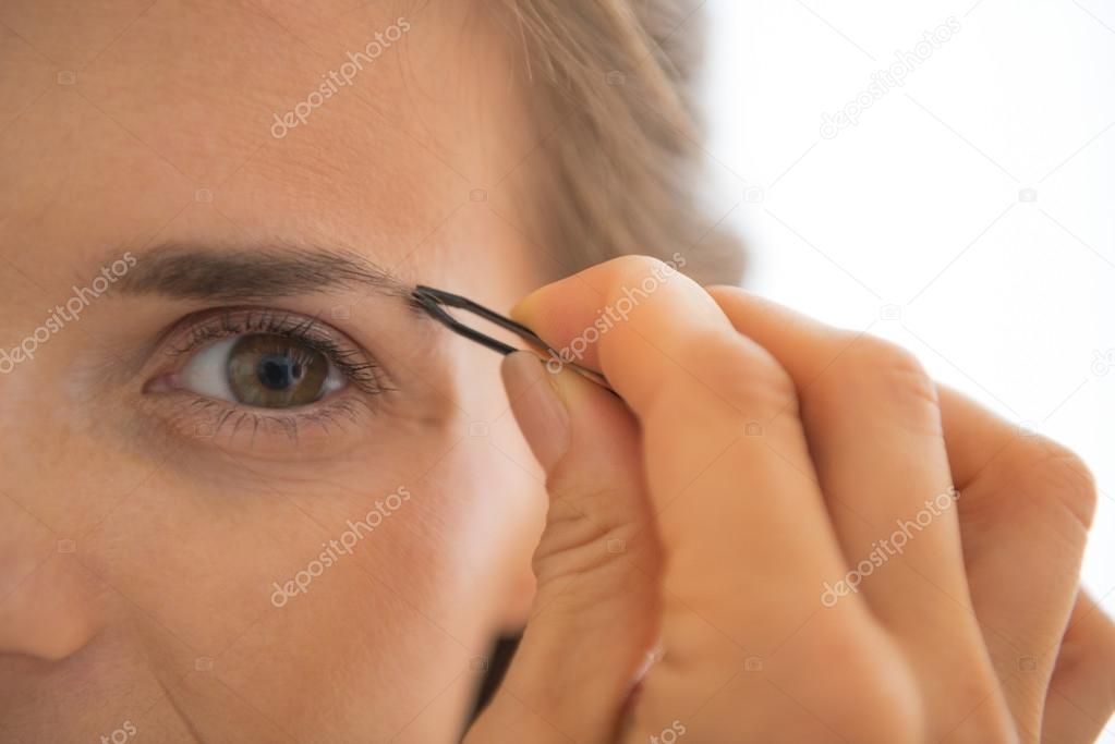 Closeup on young woman tweezing eyebrows