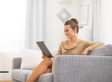 mutlu genç kadın Divan üzerinde oturan ve tablet PC'yi kullanma