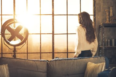 Loft daire penceresinde arayan genç kadın. arka görünüm
