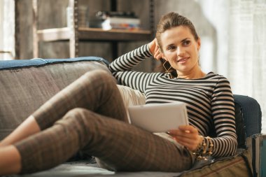 Düşünceli genç kadın kanepede içinde döşeme tablet pc ile çatı ap