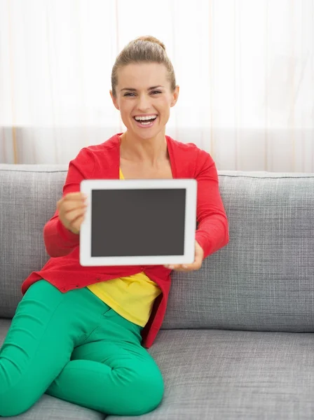 Glad ung kvinna sitter på soffan och visar TabletPC — Stockfoto