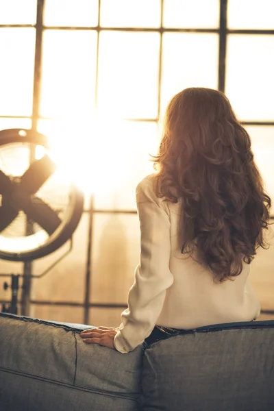 Mujer joven mirando por la ventana en el apartamento loft. visión trasera — Foto de Stock