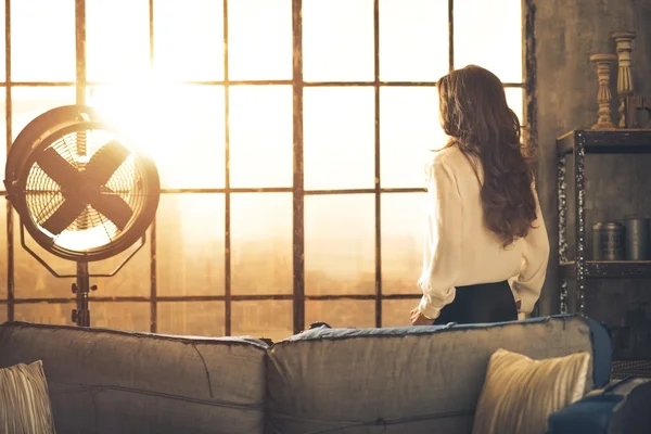 Jonge vrouw op zoek in venster in zolder appartement. Achteraanzicht — Stockfoto