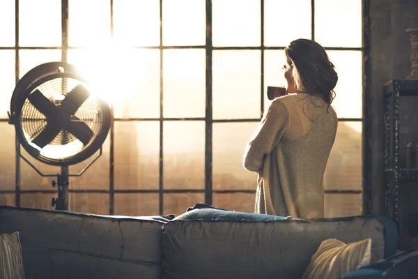 Jeune femme dégustant une tasse de café dans un appartement loft. vue arrière — Photo