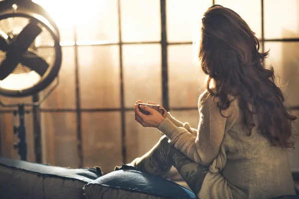 Young woman enjoying cup of hot beverage in loft apartment. rear — Stock Photo, Image