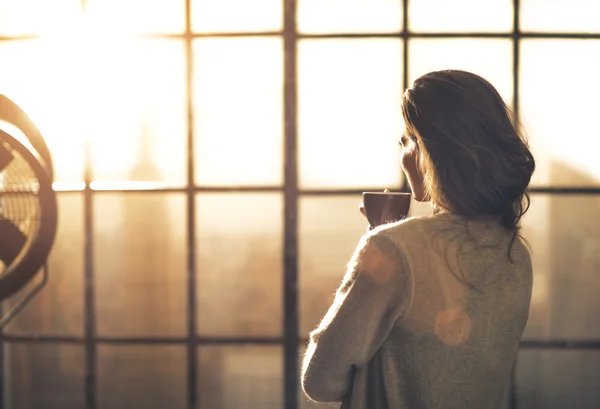 Mujer joven disfrutando de una taza de café en el apartamento loft. visión trasera — Foto de Stock