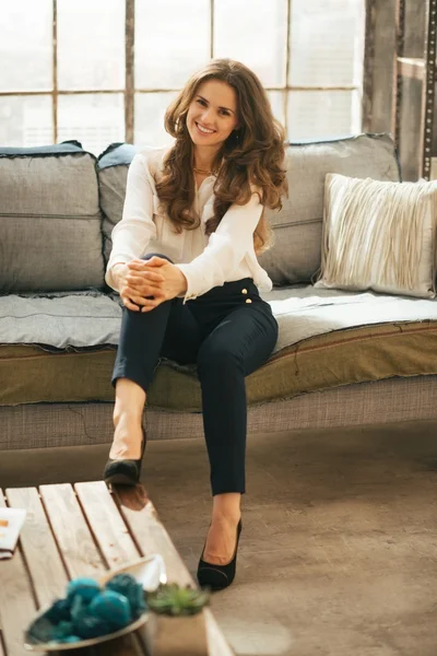 Mujer joven sonriente sentada en el sofá en el apartamento loft —  Fotos de Stock