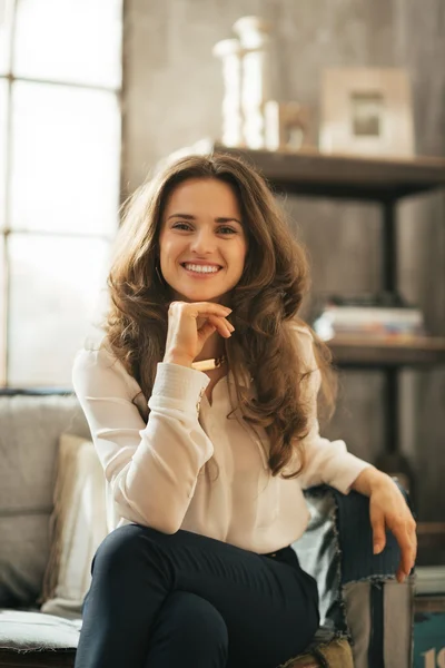 Usměvavá mladá žena sedící na gauči v Loftový byt — Stock fotografie