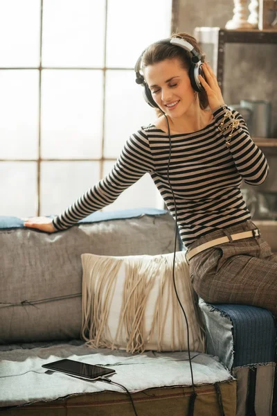 Gelukkig jonge vrouw luisteren muziek in hoofdtelefoon in loft apartmen — Stockfoto