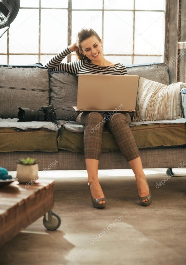 Happy young woman with dslr photo camera using laptop in loft ap