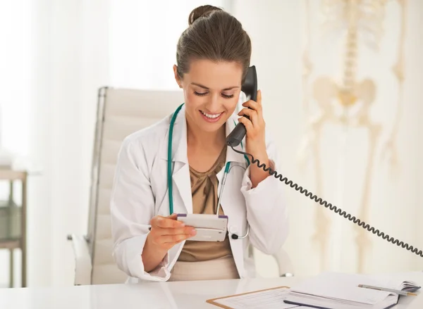 Heureuse femme médecin avec calculatrice parlant téléphone — Photo