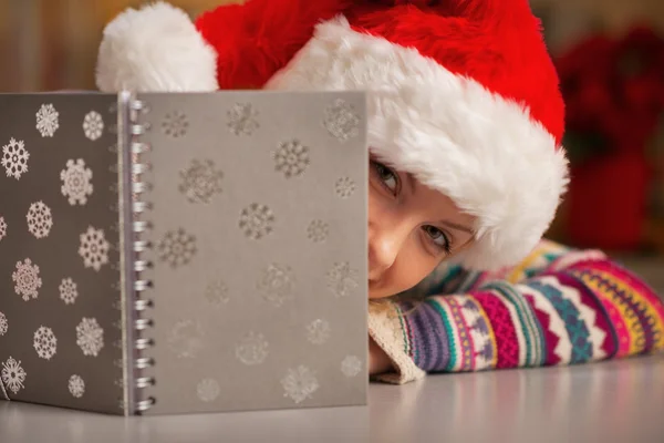 Teenager girl in santa hat looking out from notepad — Stock Photo, Image