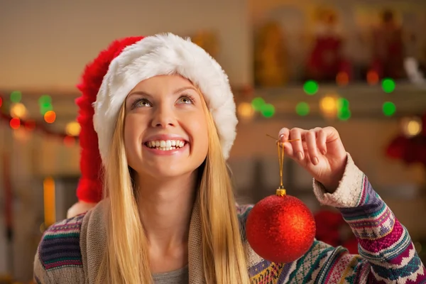 Happy teenager girl in santa hat holding christmas ball and look — Stock Photo, Image