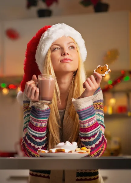Thoughtful teenager girl in santa hat with christmas cookie and — Stock Photo, Image