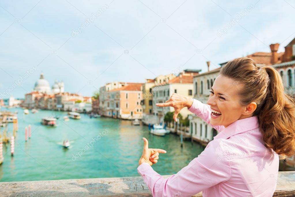 Happy young woman framing with hands while standing on bridge wi