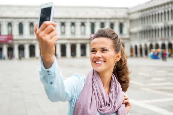 Smiling young woman taking self photo with cell phone on piazza — Stock Photo, Image