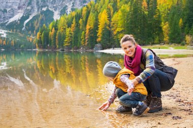 Happy mother and baby playing with water on lake braies in south clipart