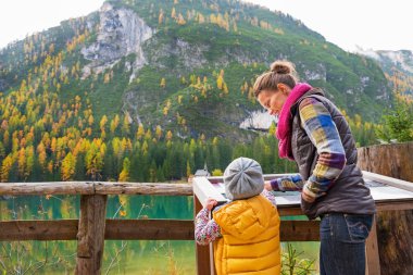 Mother and baby looking in information board while on lake braie clipart