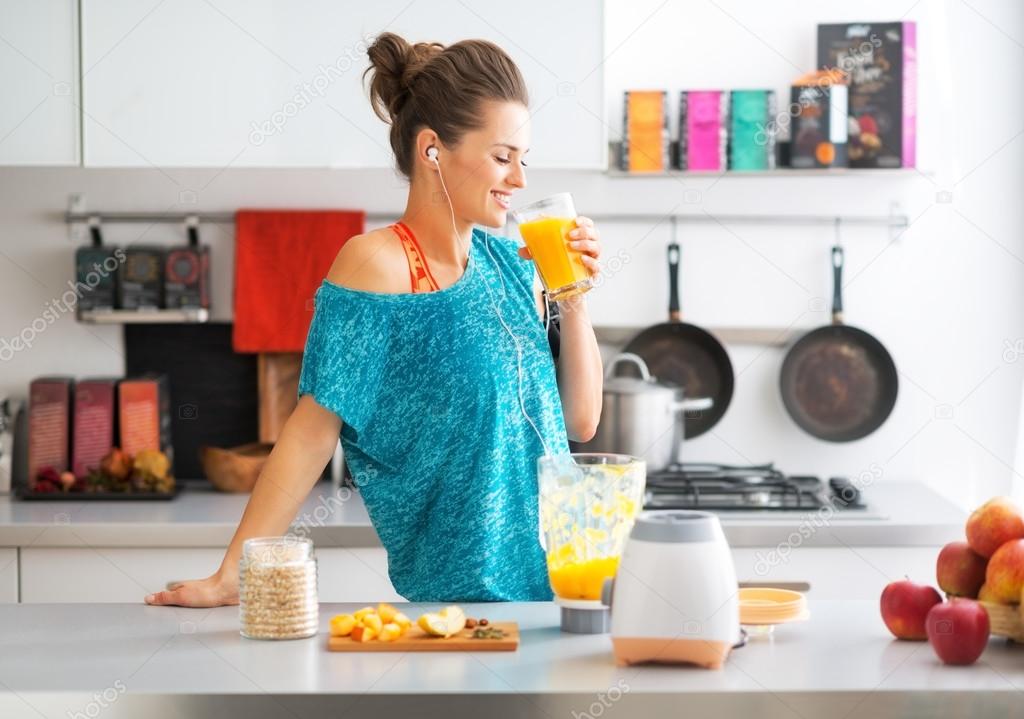 Happy fitness young woman drinking pumpkin smoothie in kitchen