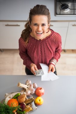 Happy young housewife with money and grocery shopping checks aft clipart