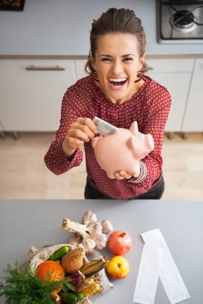 Feliz jovem dona de casa colocando dinheiro no porquinho banco depois shoppi — Fotografia de Stock